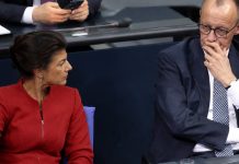 „AfD i Wagenknecht przeciwko polityce Merza. Żądają końca pomocy dla Ukrainy!” Sahra Wagenknecht w czerwonej marynarce obok Friedricha Merza w sali parlamentarnej – ilustracja AI