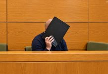 Niemcy: Zgwałcił 19-latkę i zmuszał ją do prostytucji! Sąd puścił go wolno Ilustracja AI mężczyzny zasłaniającego twarz teczką w sali sądowej