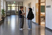 Szariat ponad szkolnymi zasadami? Ekspert ostrzega przed presją religijną w szkołach w Niemczech! Ilustracja AI: nauczycielka rozmawia z pełnoletnią uczennicą w szkolnym korytarzu