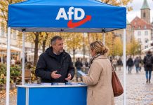 AfD dogania CDU w Badenii-Wirtembergii! Rekordowe 23 procent w nowym sondażu Dwoje dorosłych rozmawia przy punkcie informacyjnym z logo AfD – ilustracja