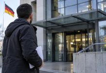 Niemcy chcą odbierać status ochronny kolejnym Syryjczykom. Najpierw pod lupę trafią młodzi mężczyźni pobierający świadczenia! Mężczyzna z dokumentami przed urzędem w Niemczech – ilustracja AI